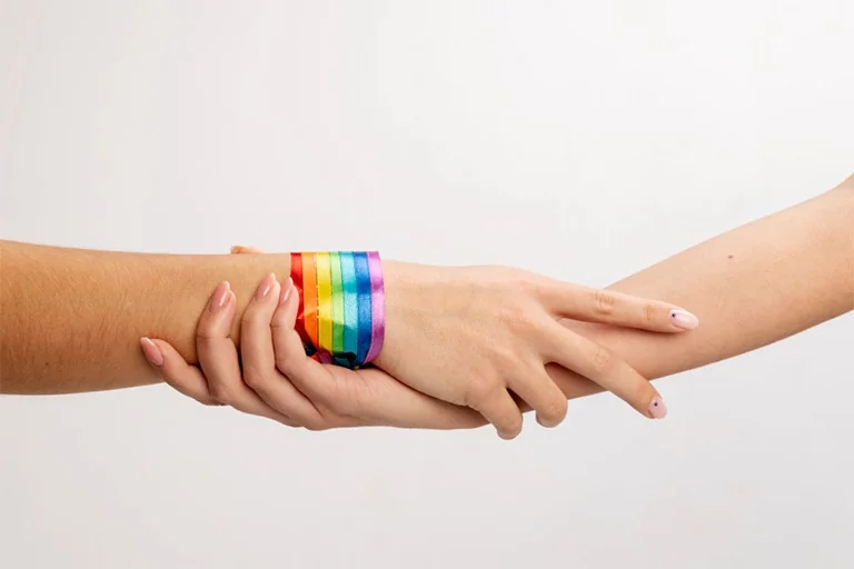 Dos manos entrelazadas, una con una pulsera de los colores del arcoíris